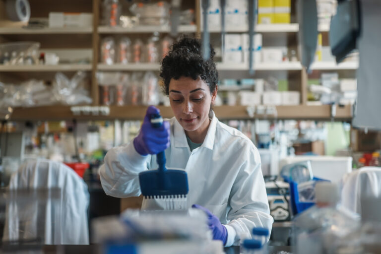 Calibr-Skaggs scientist in a white lab coat using a multichannel pipette to dispense samples into a microplate in a well-stocked lab.