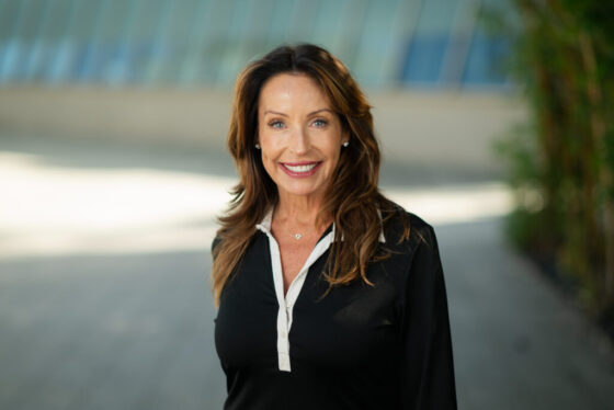 Professional headshot of Jolie Keough, Scripps Research Chief Development Officer, smiling outdoors in a black blouse with campus architecture background.