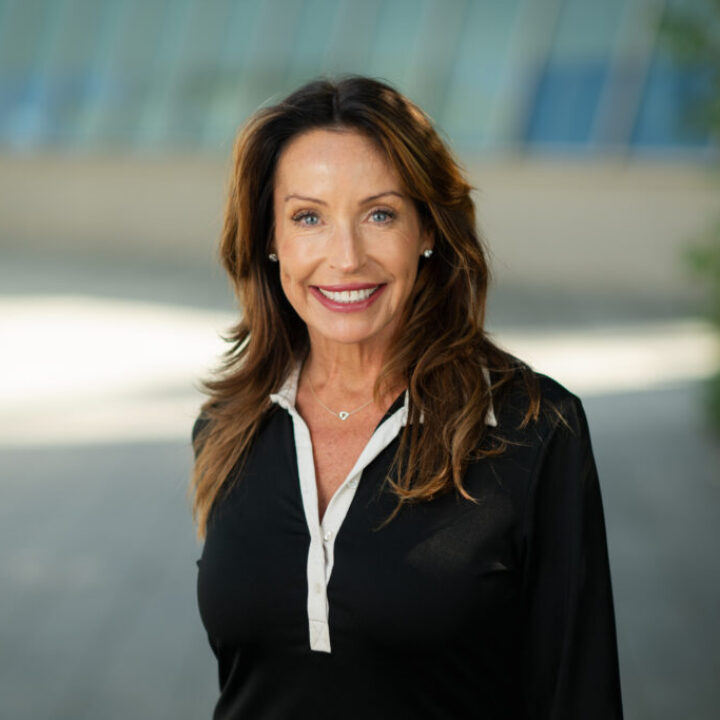 Professional headshot of Jolie Keough, Scripps Research Chief Development Officer, smiling outdoors in a black blouse with campus architecture background.