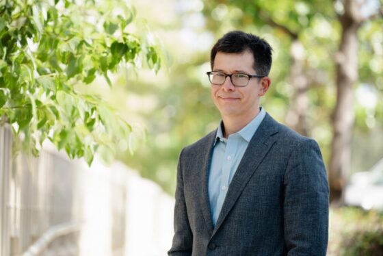 Professional headshot of Keary Engle, Scripps Research Chemistry Department Chair, in a gray blazer outdoors with green foliage background.