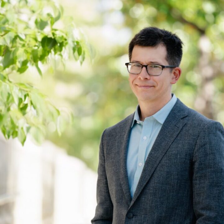 Professional headshot of Keary Engle, Scripps Research Chemistry Department Chair, in a gray blazer outdoors with green foliage background.