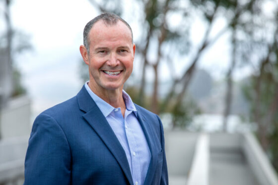 Professional headshot of Morgan Hoffman, Scripps Research Chief Philanthropy Officer, smiling in a blue blazer outdoors with campus trees in background.