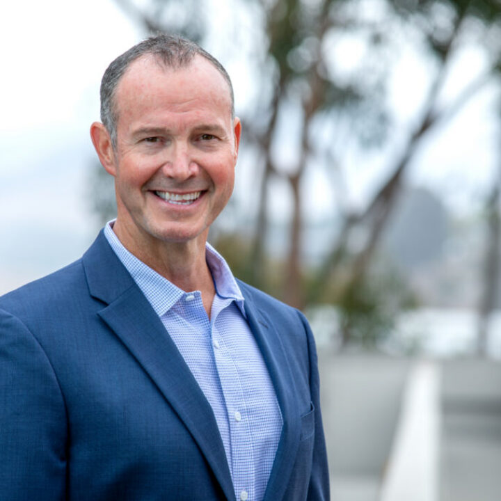 Professional headshot of Morgan Hoffman, Scripps Research Chief Philanthropy Officer, smiling in a blue blazer outdoors with campus trees in background.