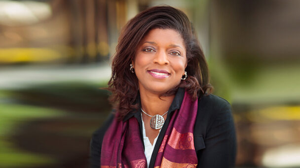 Professional headshot of Theresa Hill, SRTI Executive Committee member, outdoors in a colorful scarf with a warm background.