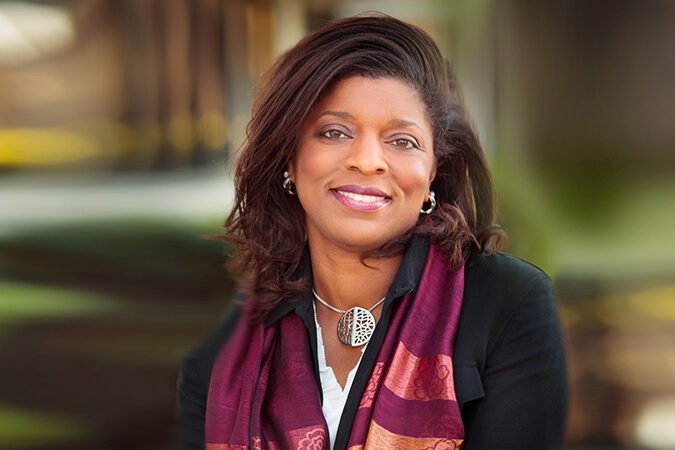 Professional headshot of Theresa Hill, SRTI Executive Committee member, outdoors in a colorful scarf with a warm background.