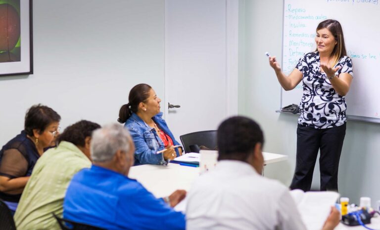 SRTI researcher presenting health education content in Spanish on a whiteboard to a group of community participants.
