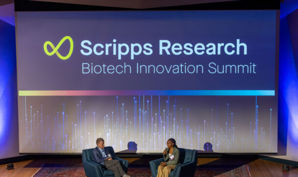 Two speakers on stage at the Scripps Research Biotech Innovation Summit in front of a large branded screen.