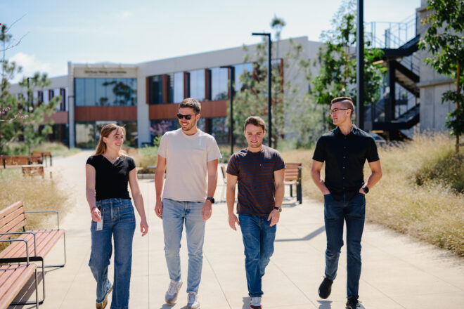 Four Scripps Research employees walking together along a campus pedestrian path on a sunny day
