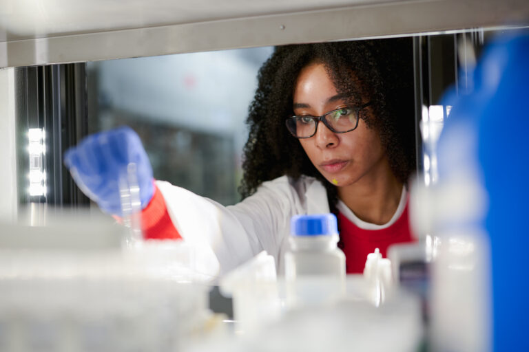 Scripps Research scientist in lab coat examining samples through laboratory glassware