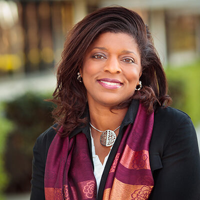 Professional headshot of Theresa Hill, SRTI Executive Committee member, outdoors in a colorful scarf with a warm background.