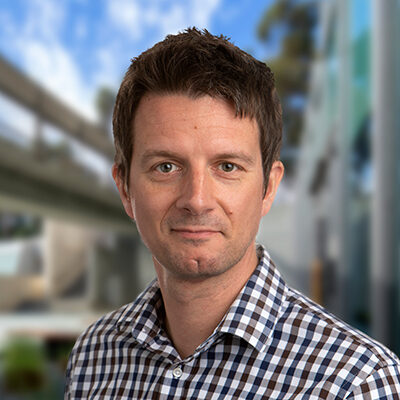 Professional headshot of Kristian Andersen, Scripps Research faculty and SRTI Executive Committee member, in a checkered shirt with campus backdrop.