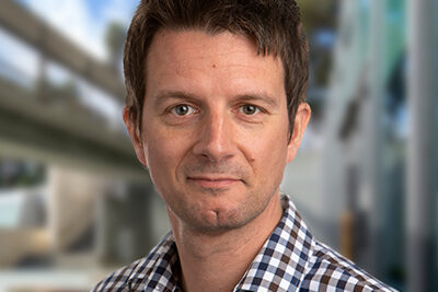 Professional headshot of Kristian Andersen, Scripps Research faculty and SRTI Executive Committee member, in a checkered shirt with campus backdrop.