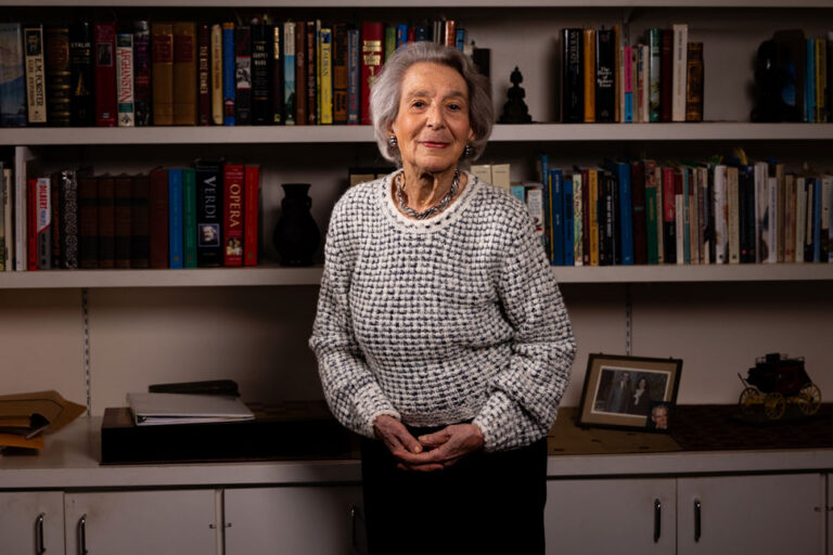 Scripps Research donor standing in front of a bookshelf filled with books, smiling at the camera