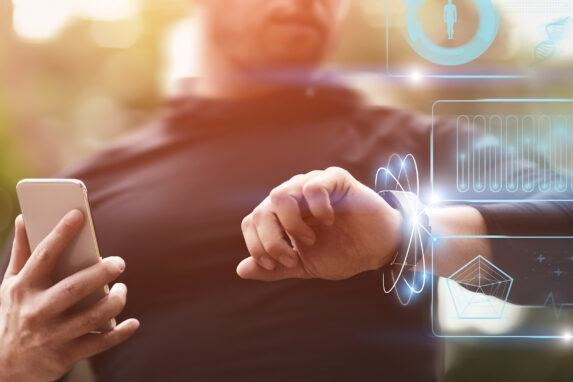 Man holding a smartphone and looking at an activity tracker on his wrist.